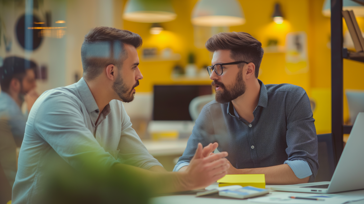 Full-thinking-Agency | © wob AG Das Bild zeigt eine Büroszene mit zwei Männern in ihren Dreißigern. Beide tragen Freizeithemden, sie sitzen an einem Schreibtisch, auf dem auch ein Laptop steht. Sie führen ein intensives Gespräch. | © wob AG