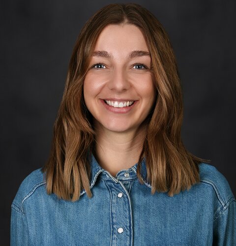 Das Bild zeigt ein Porträt von Vivien Paul. Sie ist hat schulterlange blonde Haare, trägt ein Jeanshemd und lächelt freundlich in die Kamera.