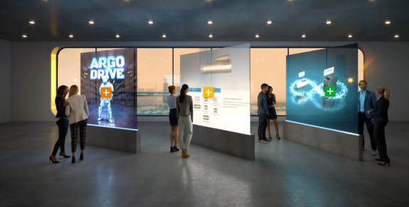 Das Bild zeigt einen Ausschnitt der Digital Experience Platform für ebm-papst. Zu sehen ist ein virtueller Ausstellungsraum. Zentrum des Ausstellungsraums sind drei interaktive Hologramme, die für Nutzende der Experience Platform Informationen zu den Produkten und Leistungen von ebm-papst liefern und außerdem klickbar sind. Letzteres ist durch kleine klickbare Kreuze gekennzeichnet, die sich auf den Hologrammen befinden. Um das Feeling einer virtuellen Ausstellung abzurunden, stehen virtuelle Personen um die Hologramme verteilt und sehen sich diese genauer an.