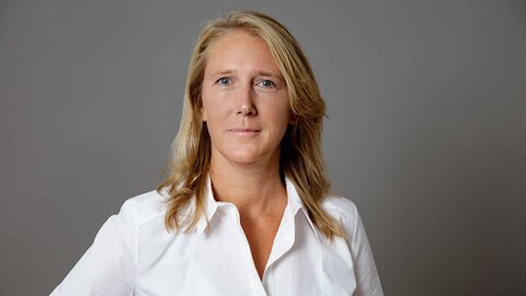 Larissa Pohl Dieses Bild ist ein Portrait von Larissa Pohl vor einem grauen Hintergrund. Sie hat blondes, schulterlanges Haar und trägt eine weiße Bluse. Sie blickt freundlich in Richtung Kamera.
