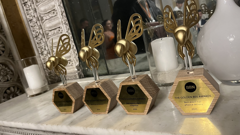 Golden Bees Zu sehen ist ein Foto von vier Awardtrophäen in Form von goldenen Biene. Die Goldenen Bienen stehen auf einem Sideboard. Auf den Plaketten der Trophäen ist das Logo von BBN zu sehen sowie die Bezeichnung „Golden Bee Awards“.